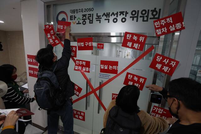 기후정의동맹과 녹색연합, 환경운동연합, 민주노총, 지역에너지전환네트워크 등 환경·노동단체 활동가 등이 15일 오전 세종시 어진동 ‘대통령소속 2050 탄소중립녹색성장위원회(탄녹위)’ 출입문에 탄녹위를 비판하는 내용의 종이를 붙이고 있다. 김정효 기자 hyopd@hani.co.kr