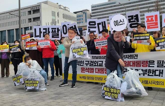 17일 서울 용산구 전쟁기념관 앞에서 열린 서울시국회의 기자회견을 마친 뒤 기시다 후미오 일본 총리 가면을 쓴 사람이 '위안부 합의이행', '독도 영유권 주장 인정', '한반도 자위대 진출' 등이 적힌 쓰레기봉투를 윤석열 대통령 가면을 쓴 이에게 건네는 퍼포먼스를 하고 있다. 연합뉴스