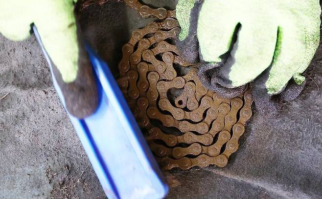 폐자전거에서 떼어 낸 체인에 슨 녹을 제거하고 있다.