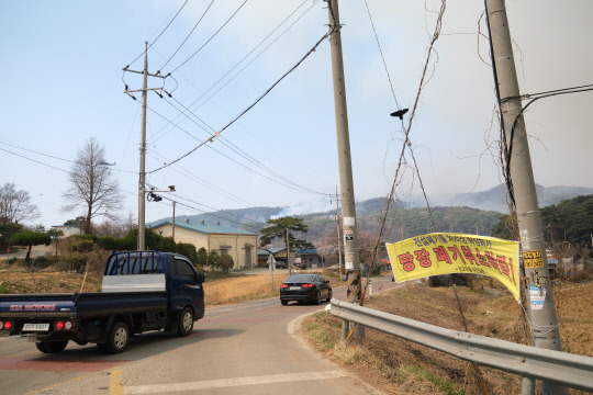 현수막이 찢어질듯 강하게 부는 바람은 산불 진화를 어렵게 만들었다. 현수막 너머로 다시 피어오르는 연기가 보인다. 사진=윤신영 기자