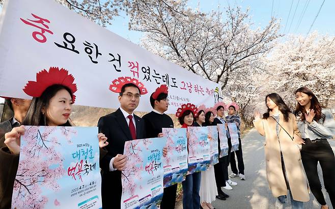 박희조 대전 동구청장(왼쪽 두번째)과 공무원들이 "중요한 건 꺾였는데도 그냥 하는 축제"라는 플래카드 아래에서 벚꽃 머리띠를 한 채 '대청호 벚꽃축제' 홍보에 나섰다. /대전 동구청