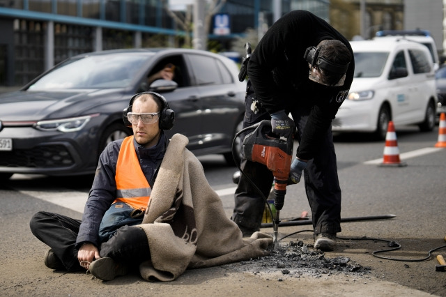 24일(현지시간) 독일 베를린에서 기후 운동가가 강력 접착제로 자신의 몸을 도로에 붙이는 도로점거 시위를 벌인 가운데 경찰이 장비를 이용해 도로 일부를 뜯어내고 있다. AP 뉴시스