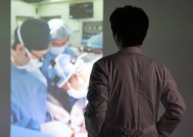 지난달 28일 한국일보를 찾은 수도권 대학병원 수술실 PA 간호사 김정환(39·가명)씨가 과거 자신이 했던 수술 장면 사진을 바라보고 있다. PA 업무는 불법인 탓에 신분을 드러내는 게 쉽지 않다. 카메라를 등지고 선 김씨가 입고 있는 흰 의사 가운은 PA 간호사 시절 병원에서 실제 착용했던 유니폼이다. 홍인기 기자
