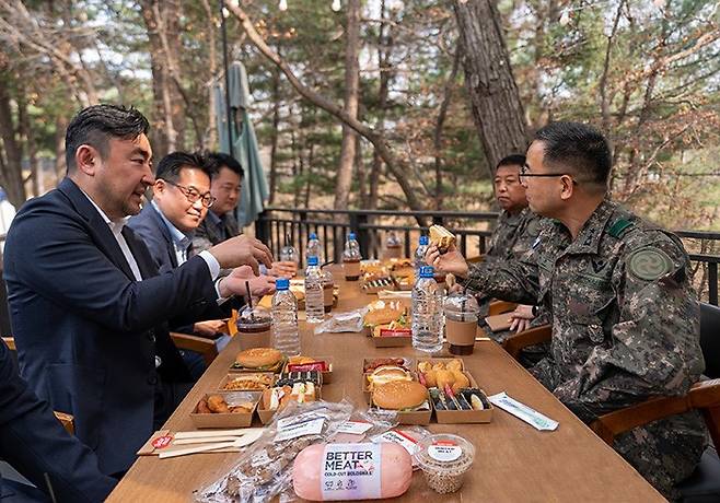 신세계푸드가 22일 경기도 동두천시 육군 28보병사단에서 장병들을 격려하기 위해 대안육 ‘베러미트(Better Meat)’로 만든 핫도그와 노브랜드 버거 전용 음료를 각 1만개씩 위문품으로 전달했다. 신세계푸드 송현석 대표(왼쪽)가 육군 28보병사단 박춘식 사단장(오른쪽)에게 ‘베러미트’로 만든 메뉴를 소개하고 있다./사진제공=신세계푸드