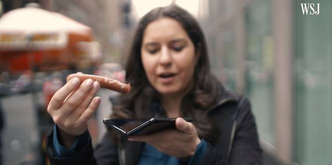 월스트리트저널(WSJ)의 테크 칼럼니스트 조안나 스턴이 삼성 폴더블폰 ‘갤럭시 폴드’에 소시지를 끼워 넣으면서 조롱하고 있다. [사진 출처 = 월스트리트저널 유튜브 영상 갈무리]