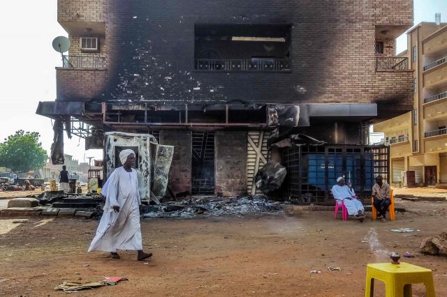 한 남성이 24일(현지시간) 수단 수도 하트룸에서 불에 탄 은행 앞을 지나가고 있다. AFP연합뉴스