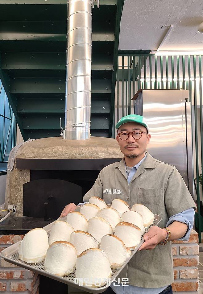 천홍원 코끼리베이글 대표가 코끼리베이글 성수점에 마련된 화덕 앞에서 매장 인기 메뉴인 ‘크림치즈 베이글’을 들고 있다. <신수현 기자>