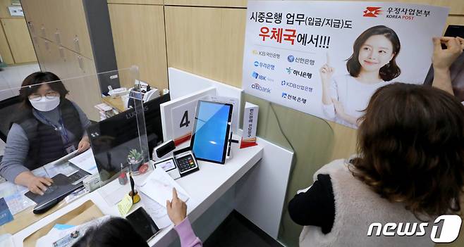 (서울=뉴스1) 장수영 기자 = 지난해 11월 30일 서울 중구 서울중앙우체국 창구에서 직원이 시중은행 입·출금 업무 안내 홍보물을 부착하고 있다. 우정사업본부는 오늘부터 별도의 수수료 없이 국민·신한·우리·하나 등 4대 은행의 예금 입·출금 및 조회할 수 있는 서비스를 시작했다. 2022.11.30/뉴스1 Copyright (C) 뉴스1. All rights reserved. 무단 전재 및 재배포 금지.