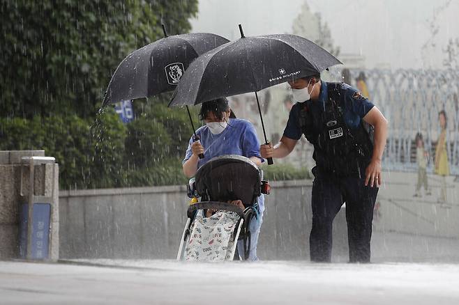 서울 종로구 세종문화회관 앞에서 한 경찰이 아이와 함께 외출한 시민에게 우산을 씌워주고 비를 피할 곳으로 안내하고 있다. 이정아 기자 leej@hani.co.kr