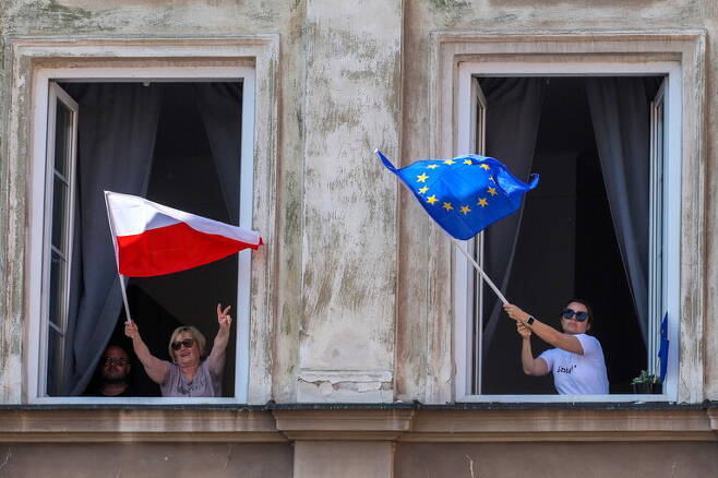 4일 폴란드 바르샤바에서 대규모 반정부 시위가 열린 가운데, 일부 시민들이 건물에서 폴란드와 유럽연합(EU) 국기를 함께 흔들고 있다. EPA 연합뉴스