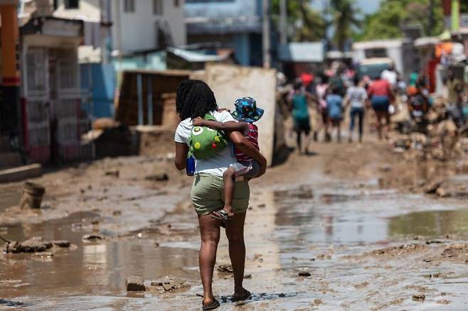 카리브해 섬나라 아이티에서 6일(현지 시각) 한 시민이 아이를 안고 폭우로 진흙탕이 된 거리를 지나가고 있다. 지난 2~4일 아이티 전국에 내린 폭우로 주요 하천과 강이 범람해 지금까지 51명이 숨지고 140명이 다쳤다. 18명은 아직 실종 상태다. [사진=레오간(아이티) EPA/연합뉴스]