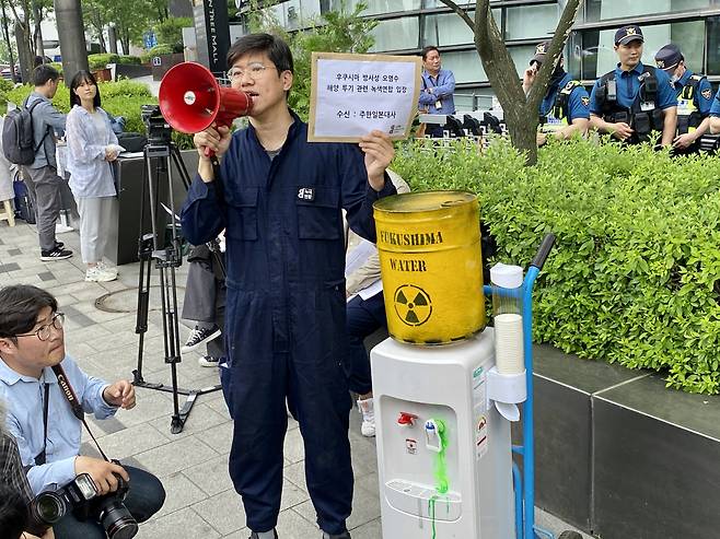 An activist from environmental group Green Korea United stages a protest in front of the Embassy of Japan in Seoul, standing next to a water purifier attached to a mock barrel of contaminated Fukushima wastewater on Wednesday.