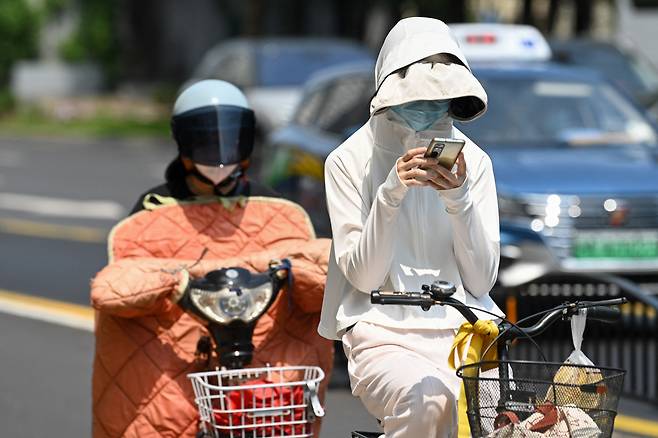 중국 상하이의 한 여성이 자외선 차단복을 입고 자전거를 타고 출근하고 있다. 상하이 기상청에 따르면 상하이의 5월 기온은 100년만에 가장 더웠다. /AFP 연합