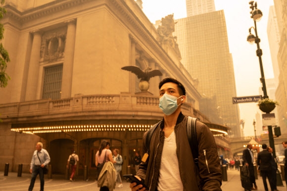 7일(현지시간) 캐나다 산불의 영향으로 미국 뉴욕의 하늘이 오렌지색으로 변한 가운데 마스크를 쓴 시민이 맨해튼 거리를 걷고 있다. 2023.6.7 AFP 연합뉴스