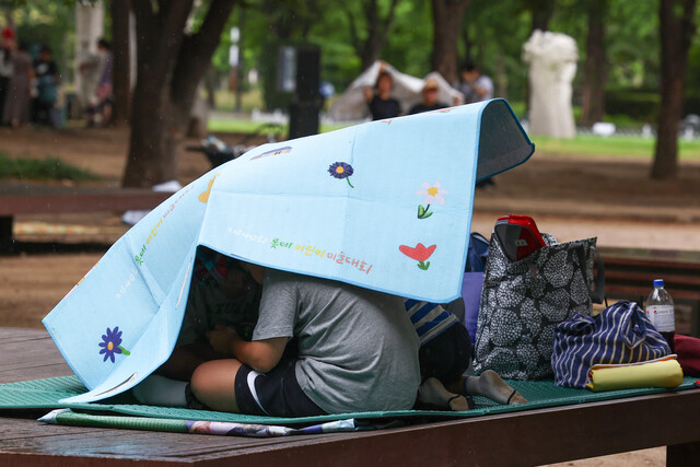 소나기가 내린 지난 6일 오후 서울 성동구 서울숲에서 휴식하던 시민들이 갑자기 내린 비에 돗자리를 우산 삼아 쓰고 있다. 연합뉴스