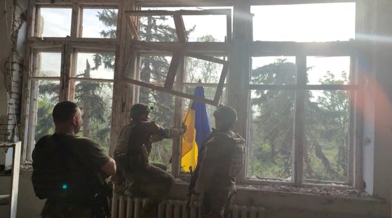 11일(현지시간) 우크라이나 동남부 도네츠크주 블라호다트네 마을의 한 건물에 우크라이나 국기를 게양하는 우크라이나 군인들. 우크라이나 군 당국은 이날 우크라이나가 러시아를 상대로 한 대공세를 시작한 지 수일 만에 동남부의 러시아 점령지 세 곳을 탈환했다고 밝혔다. [로이터=연합뉴스]