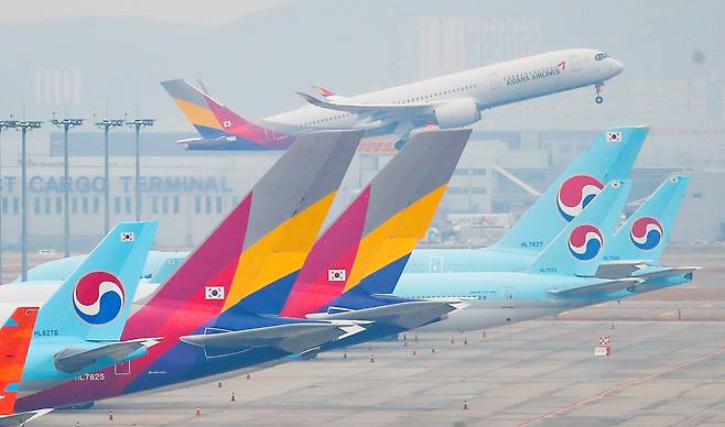 인천국제공항 주기장에 세워진 대한항공과 아시아나항공 여객기 뒤로 아시아나항공 여객기가 이륙하고 있다. [연합뉴스]