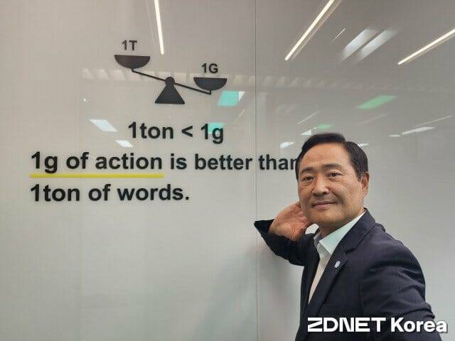 강요식 서울디지털재단 이사장이 1톤의 말보다 1그랭의 행동이 중요하다고 쓰인 슬로건을 배경으로 상암도 재단 사무실에서 포즈를 취했다.