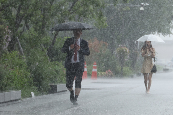 Passersby at Gwanghwamun Square in downtown Seoul walk in the rain on Thursday as heavy showers batter the nation. [YONHAP]