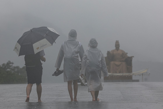 Passersby walk across Gwanghwamun Square in central Seoul barefeet on Tuesday afternoon amid the rain. [YONHAP]