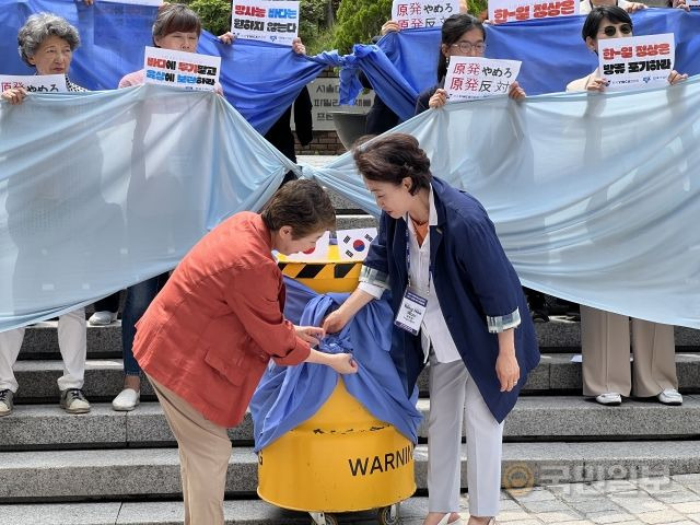 후지타니 사토코(왼쪽) 일본YWCA 회장과 원영희 한국YWCA연합회 회장이 10일 서울 중구 명동성당에서 파란 천으로 방사성 폐기물을 감싸는 퍼포먼스를 벌이고 있다.