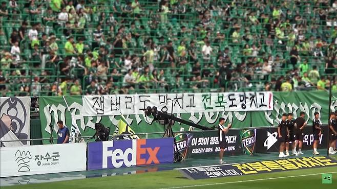 A screenshot image shows Jeonbuk Hyundai Motors FC fans with a sign that reads "Ruining Jamboree, Ruining North Jeolla Province," where the World Scout Jamboree was being held, Sunday at Jeonju World Cup Stadium in Jeonju, North Jeolla Province. (YouTube channel Jeonbuk Hyundai Sangyounggwan)
