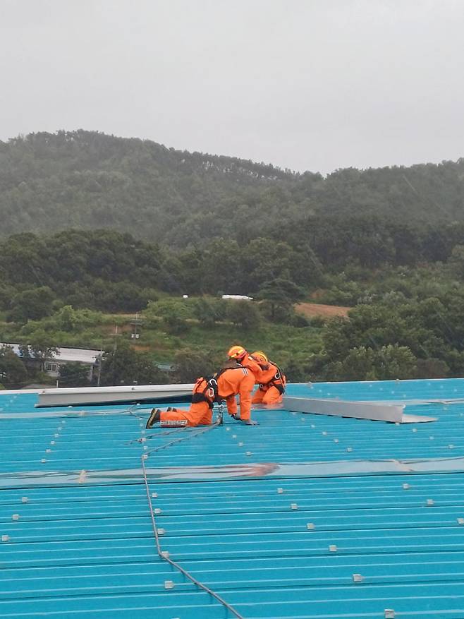 8.10.(목) 오후, 충남 공주시 월미동에서 강풍으로 건물 지붕 패널 일부가 떨어지려는 상황으로 출동한 소방대원들이 고정작업을 하고 있다.