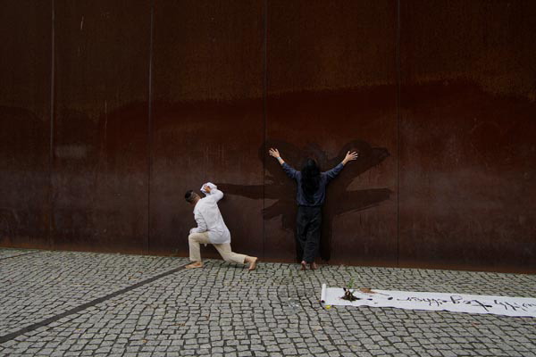 지난달 30일 독일 베를린장벽기념관에서 홍라무(오른쪽) 작가와 성백 작가가 베를린장벽을 상징하는 거대한 철판 앞에서 평화 퍼포먼스를 펼치고 있다. 아츠버스 월드투어 프로젝트 제공