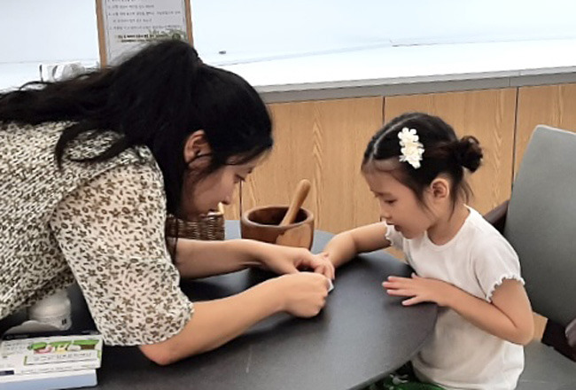 ‘한옥쉼터’ 에서 아기와 엄마 손님이 봉숭아꽃물들이기 체험을 하고 있다.