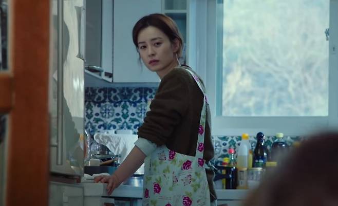 영화 '82년생 김지영'에서 극중 주인공 김지영(정유미 분)이 명절 시댁에서 앞치마를 두르고 홀로 요리하다가 거실에서 수다를 떠는 시댁 식구들을 멀리서 바라보고 있다. /사진=해당 영화 속 화면 캡처.