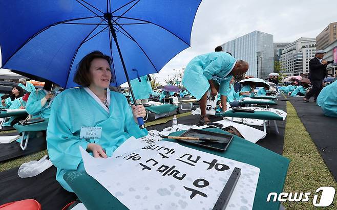 577돌 한글날인 9일 오전 서울 광화문광장에서 열린 휘호경진대회에서 참가자들이 우산으로 비를 막으며 정성스럽게 글씨를 써내려가고 있다. 2023.10.9/뉴스1 ⓒ News1 이동해 기자