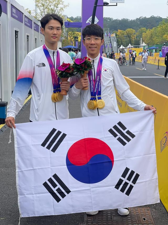 김정빈(왼쪽)이 경기 파트너 윤중헌과 함께 27일 중국 항저우에서 열린 2022 항저우 장애인 아시안경기대회 시각장애 69㎞ 개인 도로에서 우승한 뒤 이번 대회에서 수확한 3개의 금메달을 목에 걸고 태극기를 활짝 펴들고 있다. 대한장애인체육회 제공