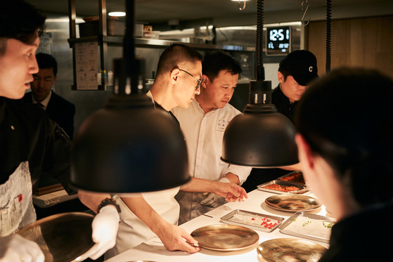 Kang Min-goo of Mingles, left, and Shin Chang-ho of Joo Ok are inside the kitchen cooking the new dishes they have created for the Korean Food Promotion Institute, on Nov. 3 at Mingles in Gangnam District, southern Seoul. [KOREAN FOOD PROMOTION INSTITUTE]