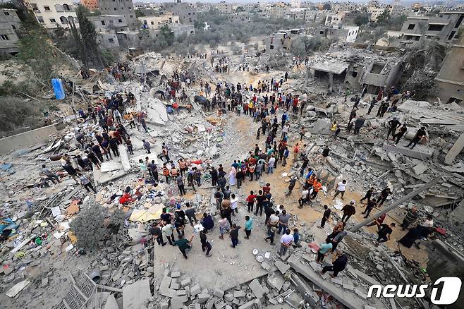 12일(현지시간) 이스라엘의 공격으로 무너진 가자지구 칸 유니스 지역의 건물 사이로 구조대원들과 주민들이 서있다. 2023.11.13 ⓒ AFP=뉴스1 ⓒ News1 정지윤 기자