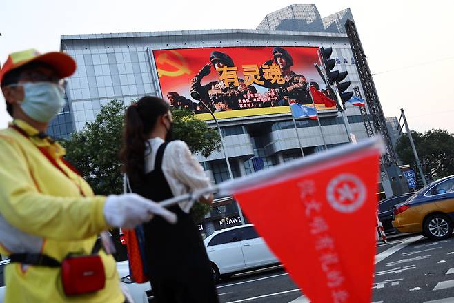 중국의 한 자원봉사자가 2022년 8월 2일 중국 베이징에서 중국 인민해방군(PLA) 군인들의 모습이 보이는 스크린 근처에서 보행자들을 위해 교통을 지도하고 있다. 로이터