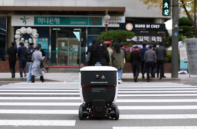 서울 강남구 코엑스 인근 횡단보도를 건너고 있는 배달 로봇 ‘딜리’. 가로 55㎝, 세로 71㎝, 높이 78㎝ 직육면체 형태에 바퀴 6개가 달렸다. 로봇 상단의 뚜껑을 열면 2ℓ 생수를 6개까지 넣을 수 있다. 로봇에는 주변 사물을 인식하는 ‘라이다’(LiDAR)가 달려 있어 행인과 자동차를 피해 이동하고, 빨간불이 켜진 건널목에선 신호가 바뀔 때까지 기다리기도 한다. 딜리는 코엑스 인근 6개 건물에 음식을 배달하고 있다./뉴시스