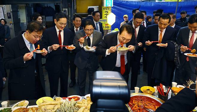 윤석열 대통령(가운데)과 재벌 총수들이 2023년 12월6일 부산 중구 깡통시장에서 떡볶이를 먹고 있다. 왼쪽부터 최재원 SK 수석부회장, 이재용 삼성전자 회장, 조현준 효성 회장, 윤 대통령, 구광모 LG 회장, 김동관 한화 부회장, 정기선 HD현대 부회장. 연합뉴스