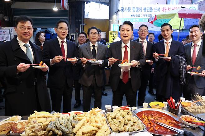 윤석열 대통령이 6일 부산 중구 깡통시장에서 기업 총수들과 함께 떡볶이 튀김 빈대떡을 시식하는 모습. 오른쪽 부터 정기선 HD현대 부회장, 김동관 한화그룹 부회장, 구광모 LG그룹 회장, 윤 대통령, 조현준 효성그룹 회장, 이재용 삼성전자 회장, 최재원 SK수석부회장 ⓒ 연합뉴스