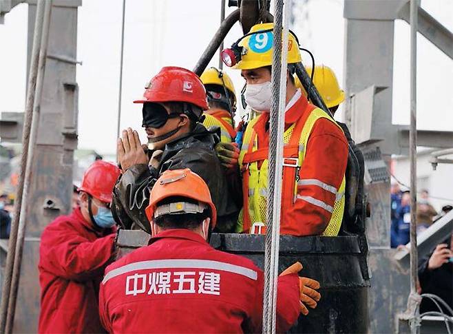 광부의 감사 인사 - 중국 산둥성 옌타이시 우차이룽 금광 폭발 사고로 지하에 갇혔던 한 광부(가운데 안대 쓰고 있는 사람)가 2주 만에 구출된 뒤 두 손을 모아 구조대에 감사 인사를 하고 있다. 안대를 한 것은 갑자기 밝은 빛에 노출돼 눈이 손상되는 것을 막기 위해서다. 이날 지하에 갇힌 광부 22명 중 11명이 구출됐다. /로이터 연합뉴스