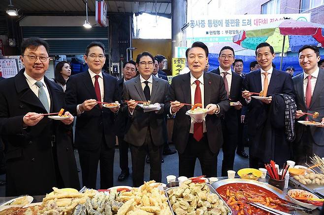 윤석열 대통령이 지난 6일 부산 국제시장에서 기업 총수들과 함께 떡볶이, 튀김 등을 먹고 있다. 오른쪽부터 정기선 HD현대 부회장, 김동관 한화그룹 부회장, 구광모 LG그룹 회장, 윤 대통령, 조현준 효성그룹 회장, 이재용 삼성전자 회장, 최재원 SK수석부회장. /연합뉴스