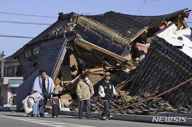 [와지마=AP/뉴시스] 2일 일본 이시카와현 와지마시에서 소지품을 꾸린 한 가족이 전날 노토반도에서 발생한 지진으로 무너진 한 가옥 앞을 지나가고 있다. 기시다 후미오 일본 총리는 비상재해대책본부 회의를 열고 "이재민의 구명·구조는 시간 싸움"이라며 "주민 안전 확보를 최우선으로 전력을 다해줄 것"을 주문했다. 2024.01.02.
