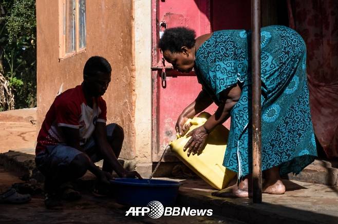 카숨바 데니스가 2023년 5월 22일(현지시각) 그의 할머니 에디슨 난테자가 부어주는 물을 대야에 받고 있다. /AFPBBNews=뉴스1