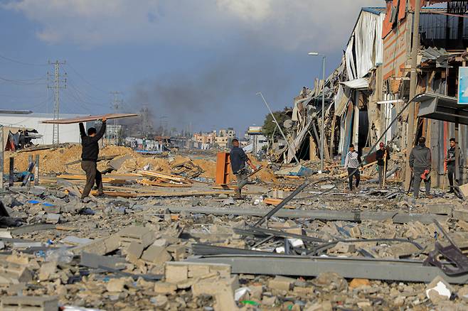 14일(현지시간) 팔레스타인 가자지구 중부 도시 데이르엘발라에서 주민들이 이스라엘군의 공습으로 폐허가 된 건물 밖을 지나고 있다. 신화연합뉴스