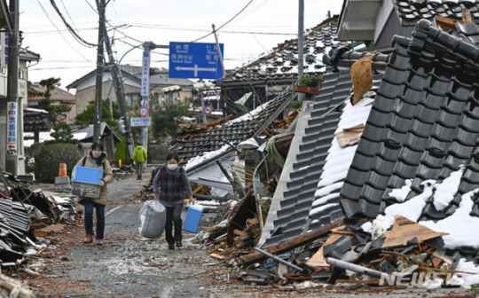 지난 11일 일본 이시카와현 스즈시에서 사람들이 지진으로 무너진 집 앞을 지나가고 있는 모습. AP뉴시스