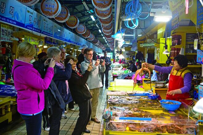 중구 연안부두에 있는 인천종합어시장에서 한 상인이 수산물을 들어보이자 외국인 관광객들이 신기한 듯 사진을 찍고 있다 . 인천관광공사 제공