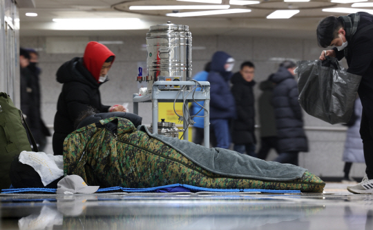 지난달 23일 서울 중구 서울역 지하도에서 자원봉사자들이 노숙인에게 따뜻한 물과 핫팩을 나눠주고 있다. 뉴시스