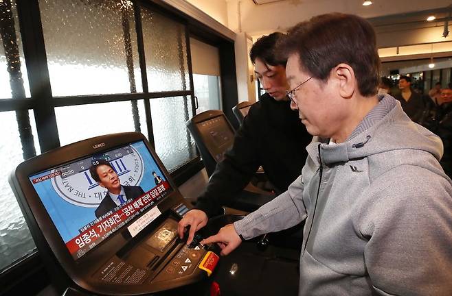 이재명 더불어민주당 대표가 28일 은평구 한 헬스장에서 직장인 정책간담회 전 런닝머신을 하고 있다. 러닝머신 화면에 같은 시간 국회 소통관에서 공천 관련 기자회견 중인 임종석 전 대통령 비서실장 뉴스가 나오고 있다./ 사진=연합뉴스