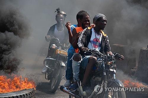 (AFP=연합뉴스) 아이티 남성들이 12일(현지시간) 최악의 소요 사태 와중에 타이어가 불타고 있는 수도 포르토프랭스의 도로를 오토바이를 타고 질주하고 있다.