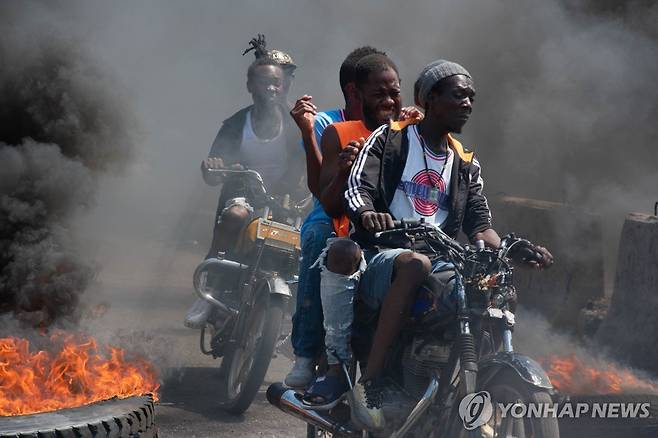 연기를 뚫고 질주 (포르토프랭스 AFP=연합뉴스) 12일(현지시간) 포르토프랭스에서 오토바이를 탄 주민들이 불타는 타이어에서 뿜어져 나오는 화염을 지나 이동하고 있다. 2024.3.15