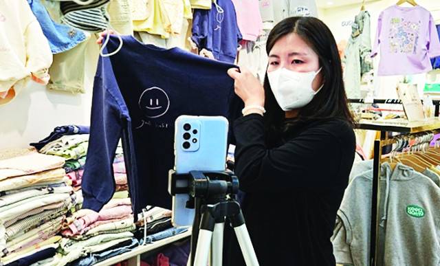 한 아동복 판매 상인이 지난 15일 서울 중구 남대문시장 아동복 거리에서 휴대폰을 활용한 ‘라이브 커머스’ 방송으로 신상 아동복을 선보이고 있다.